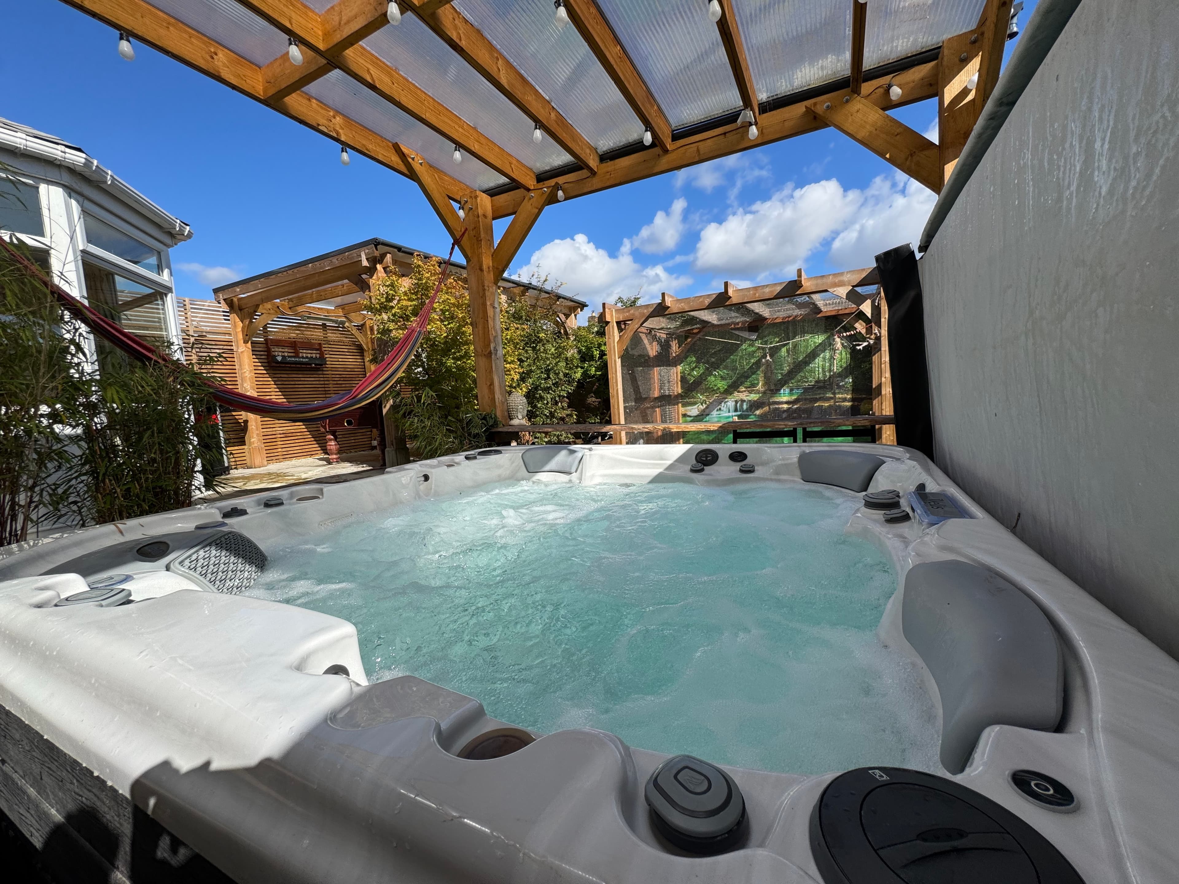 The hot tub bubbling under the cedar pergola, with the hammock and garden pergolas beyond